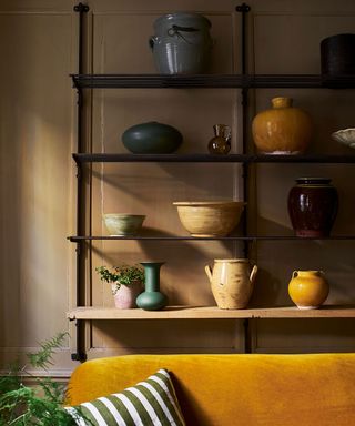 ochre velvet sofa with shelving display of ceramic vessels