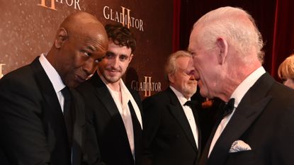 Denzel Washington wears a black suit while shaking hands with King Charles who is wearing a tuxedo