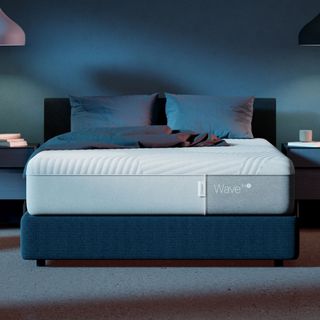 Casper Wave Hybrid Snow Mattress on a bed with pillows against a blue wall.