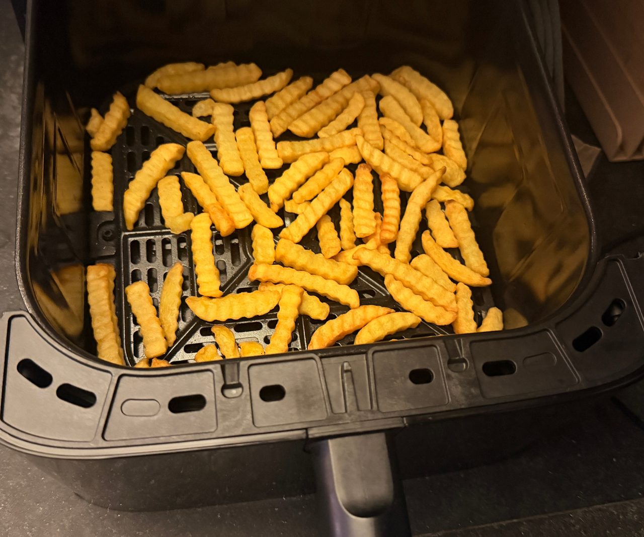 Crinkle cut fries in a flat layer over the base of an air fryer basket.