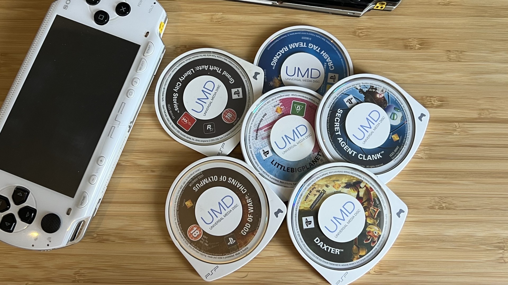 PSP UMDs arranged on a wooden desk with a white PSP handheld in the corner