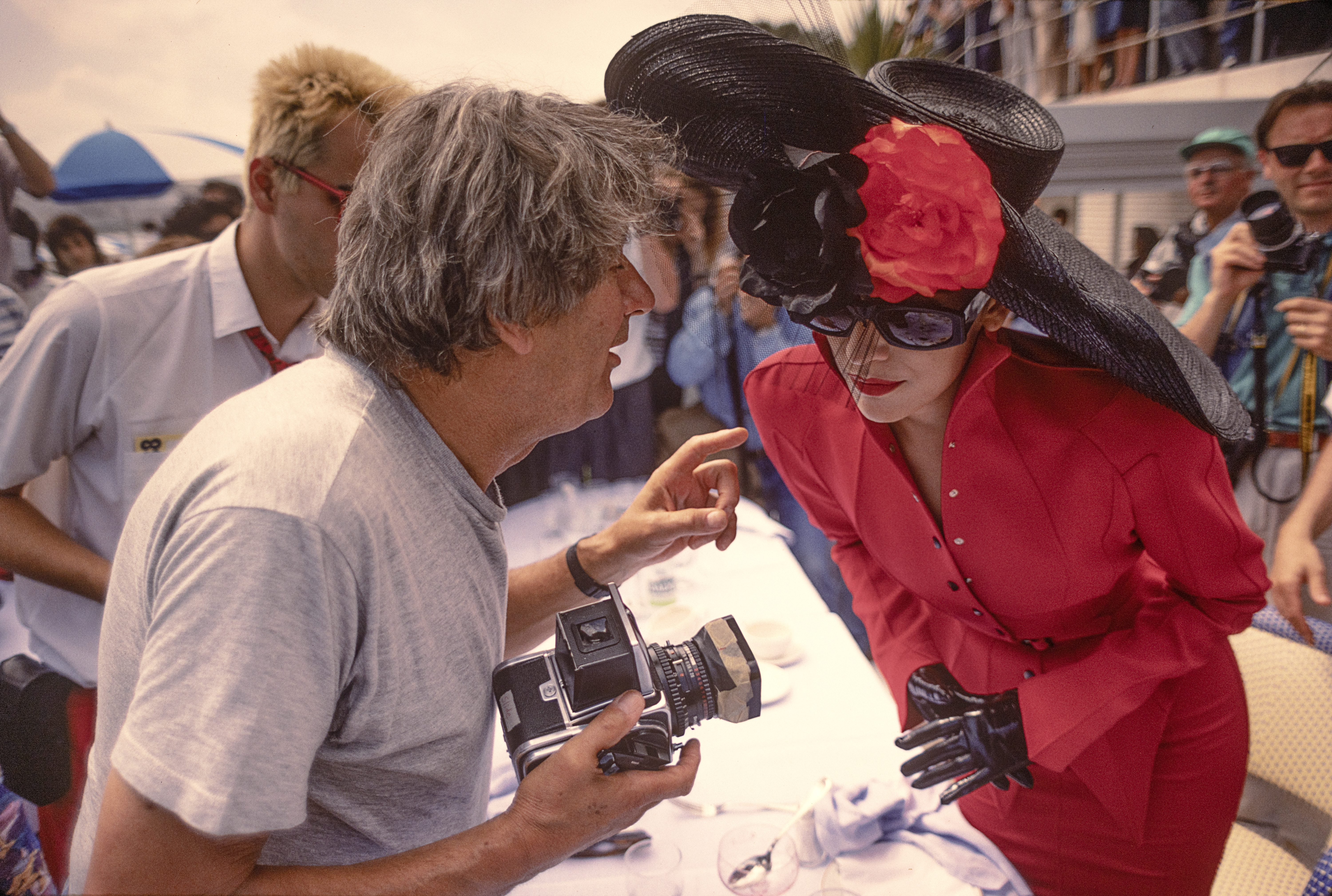 Photographer Helmut Newton talks to a model in red dress and a hat