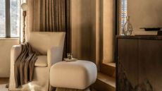 A sandy beige living room with minimalist furniture and a gilded standing lamp, a sideboard holding an empty vase and a bowl