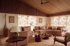 a retro living room with a timber clad roof and a pink curved sofa with patterned sheers