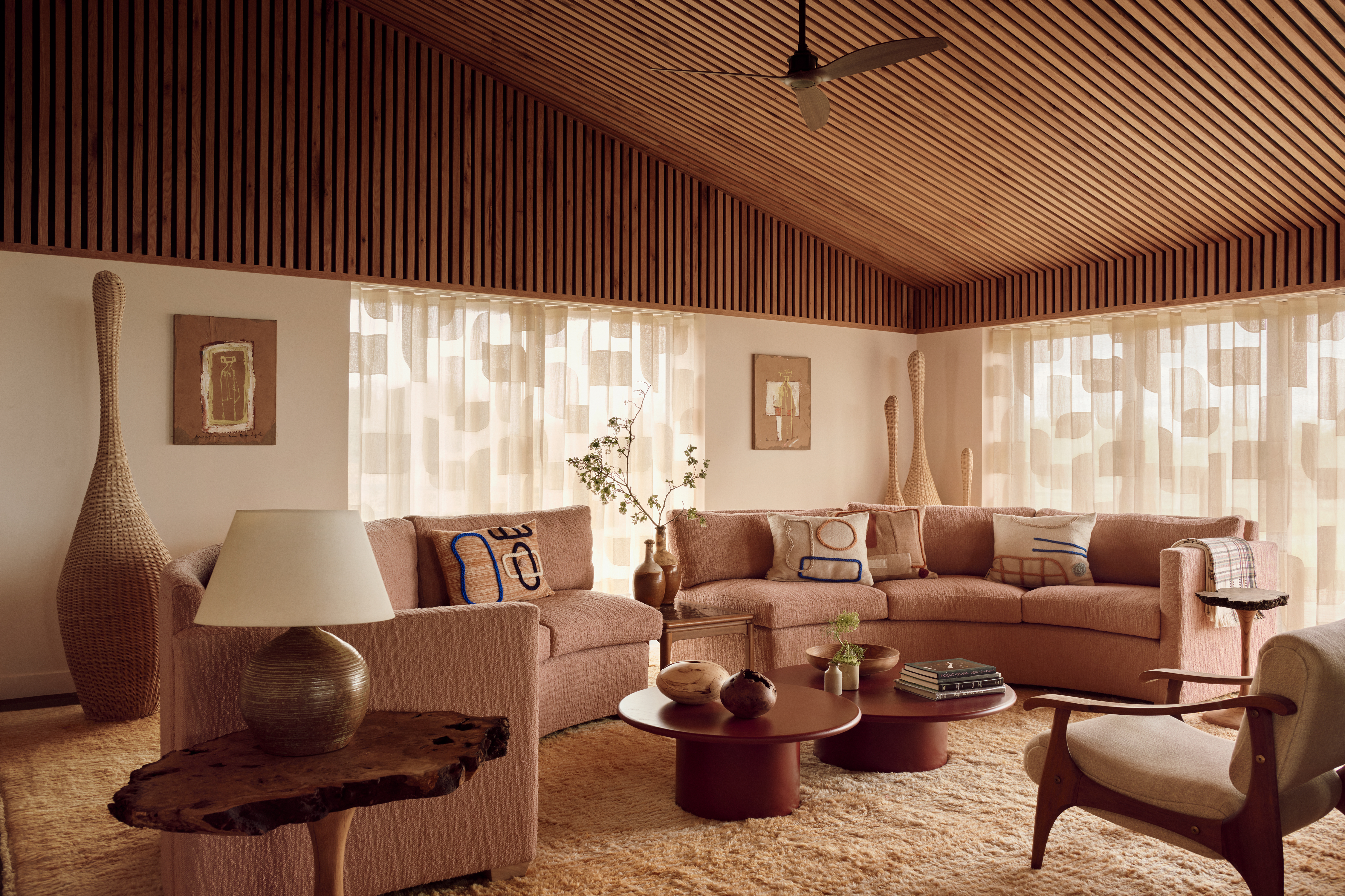 a retro living room with a timber clad roof and a pink curved sofa with patterned sheers