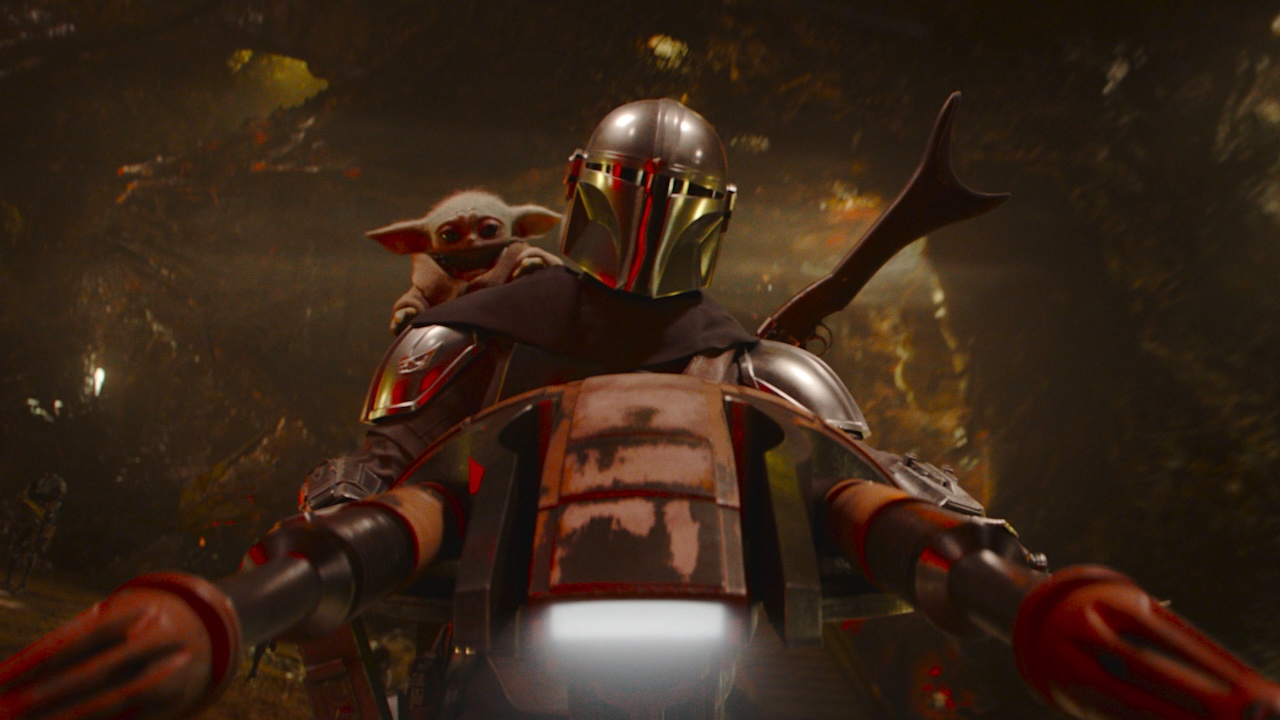 The Mandalorian driving a red hovercraft while holding Grogu in The Mandalorian and Grogu