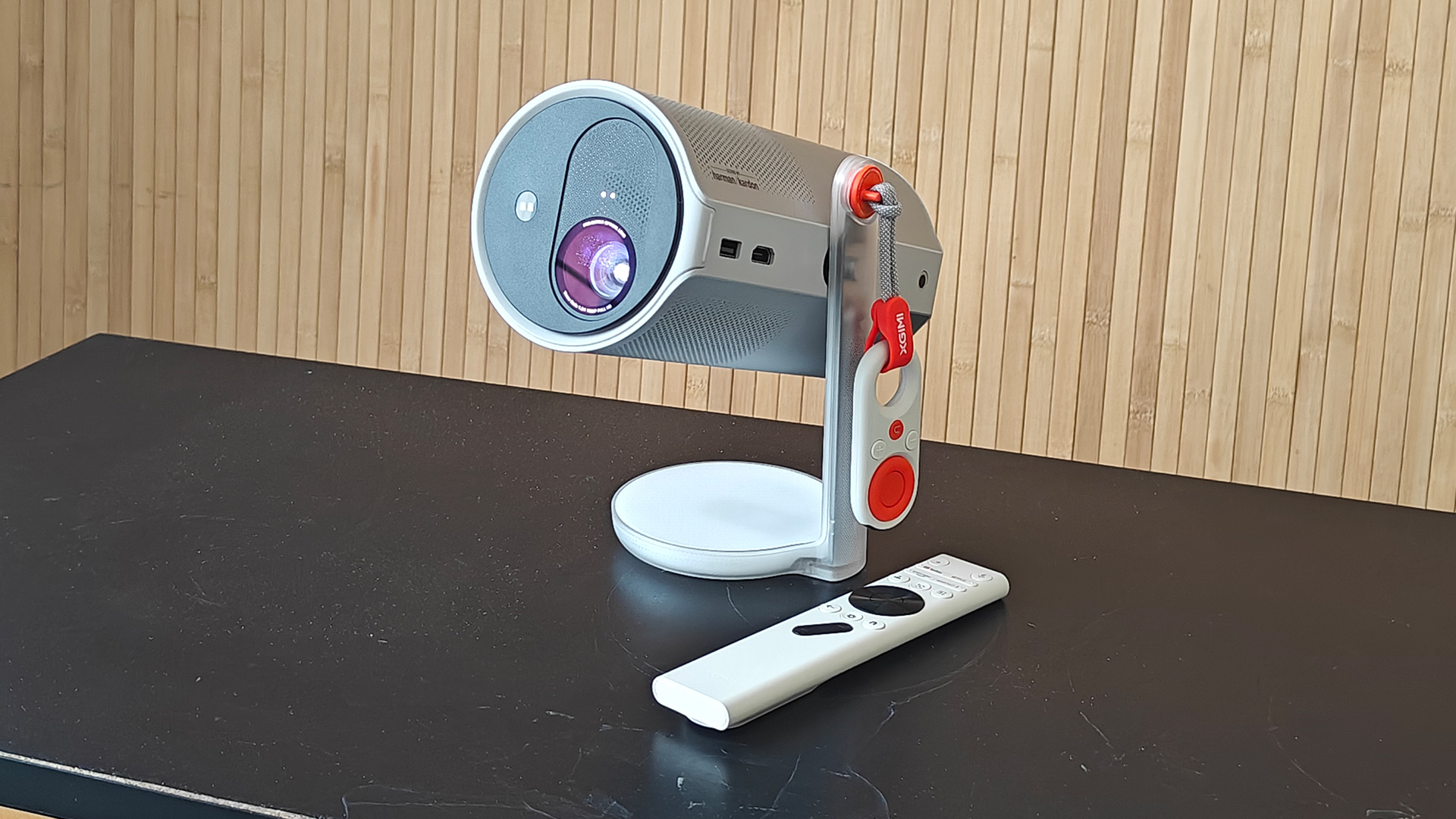 Xgimi MoGo 4 portable projector on black surface in front of wooden wall with remote control next to it