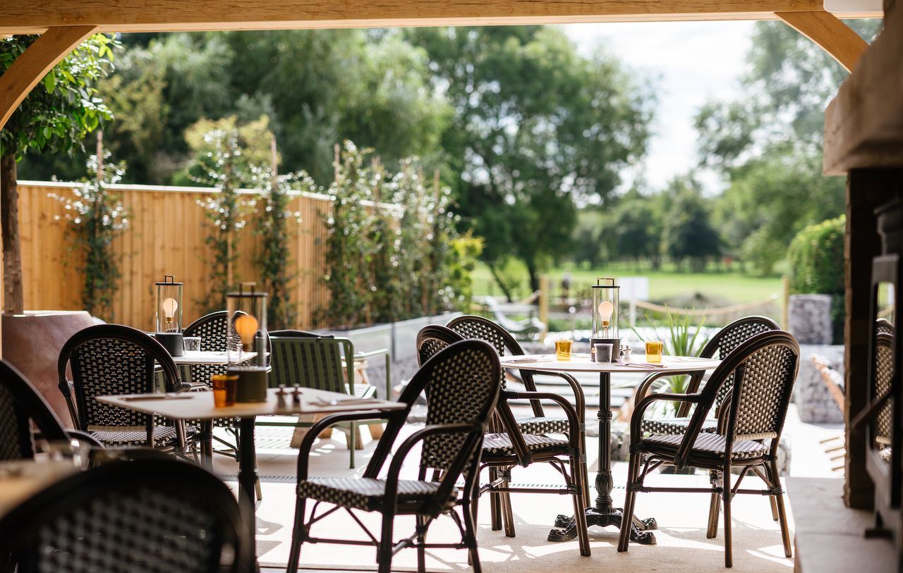A hotel restaurant with wicker cafe-style seating overlooking a golf course