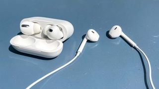 The Apple AirPods Pro in their charging case plus the EarPods, side by side on a blue table