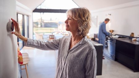 A woman adjusting a smart thermostat on the wall