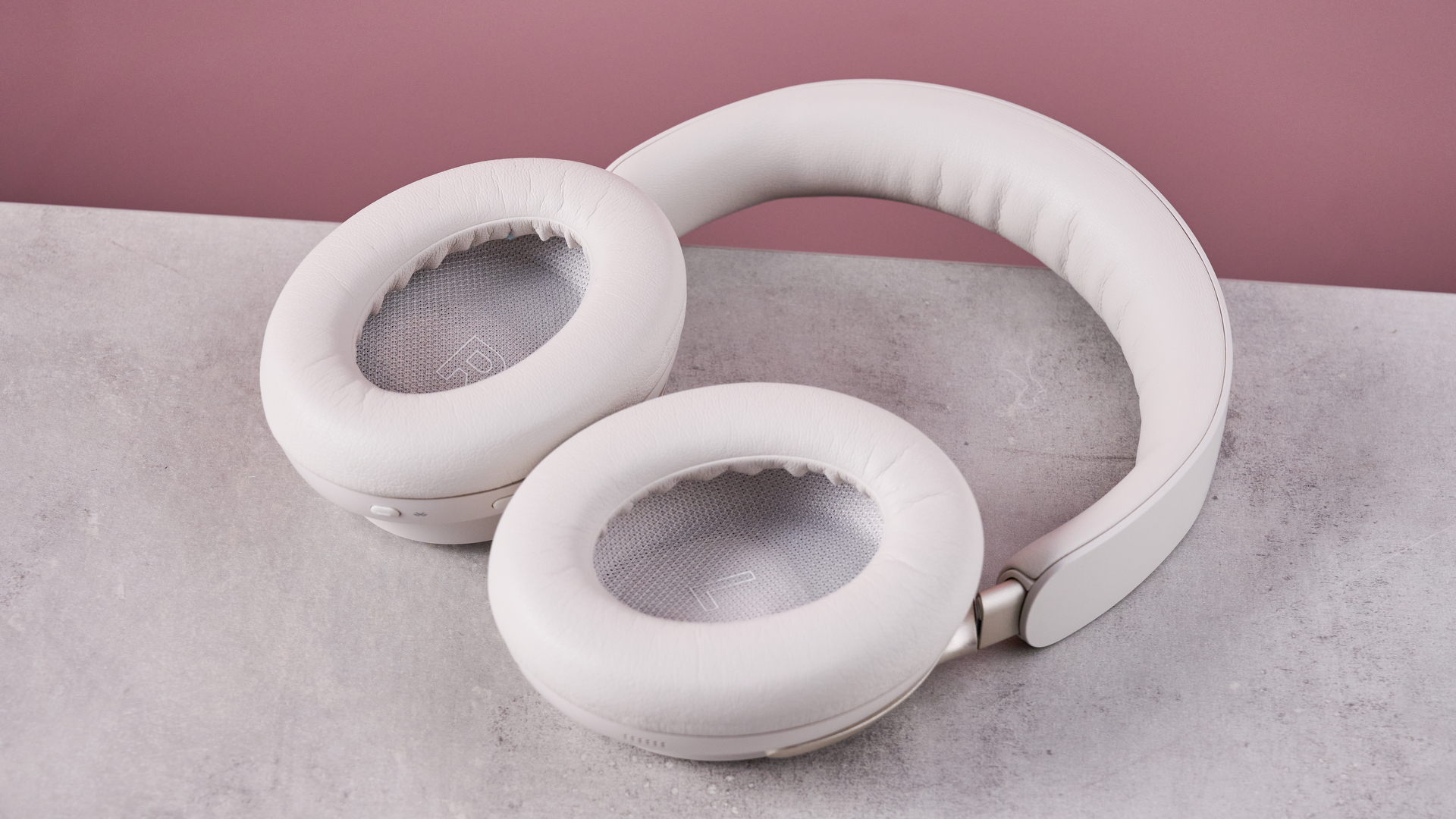 Bose QuietComfort Ultra Headphones on a gray surface with a pink background, showing the inside of the earcups