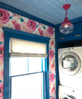 Bright laundry room with bold botanical wallpaper on wall, complementary blue patterned wallpaper on ceiling, and blue painted woodwork