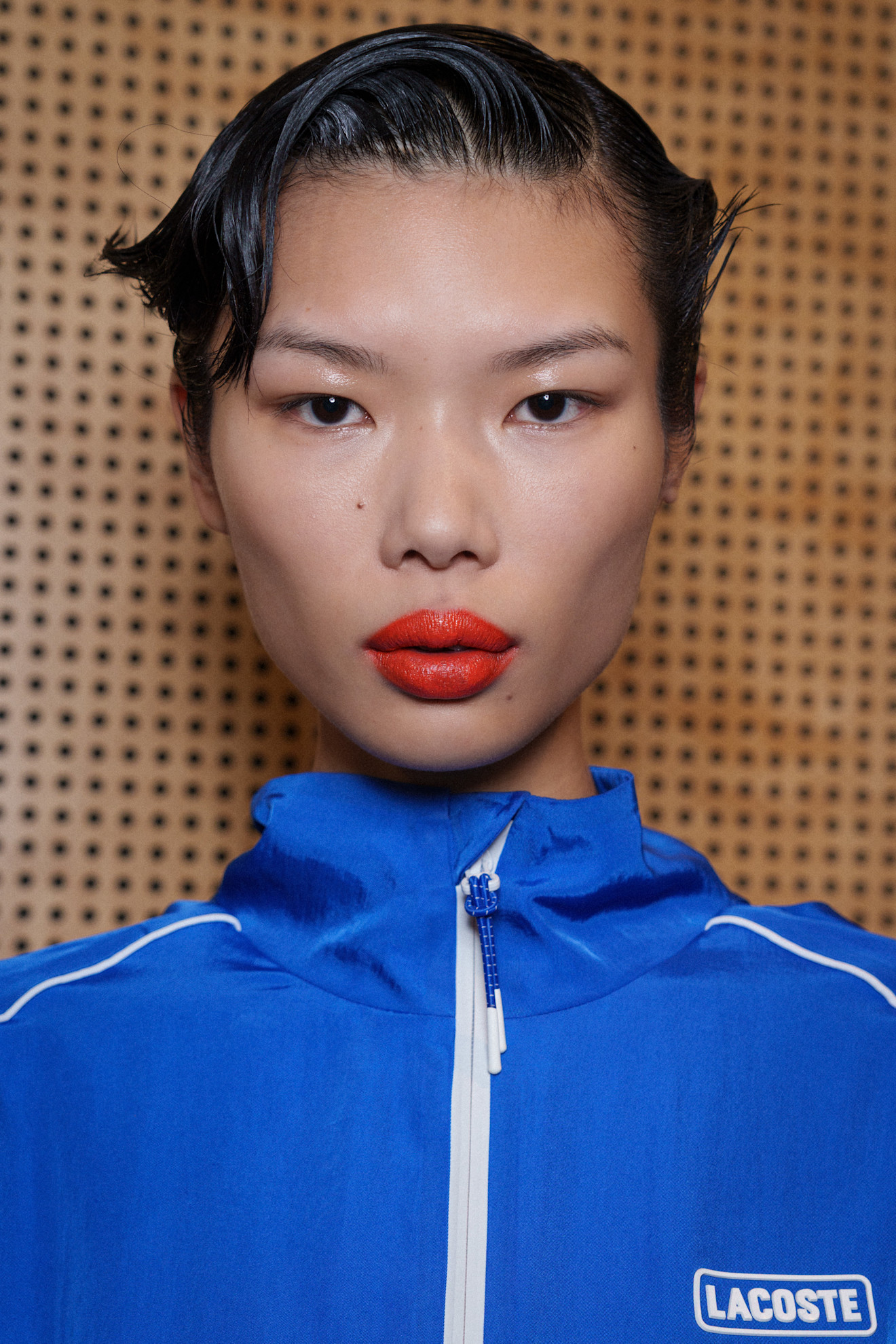 A model at the Lacoste spring-summer 26 fashion show wearing a bold reddish orange lipstick.