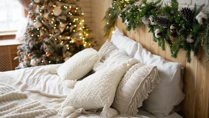 a Scandinavian style bedroom with a white bed, wooden headboard, and a christmas tree and garland above the bed