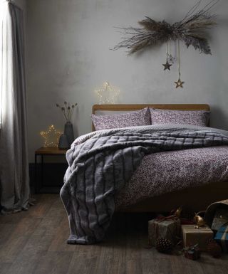A grey bedroom with concrete effect wall decor, DIY Christmas decoration above bed, grey faux fur throw and star LED lighting decor
