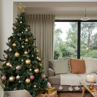 A neutral-coloured living room with a Christmas tree next to the sofa decorated with metallic baubles