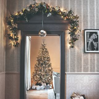 A doorway decorated with a Christmas pre-lit garland leading to a room with a Christmas tree