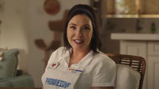 Stephanie Courtney smiles as she sits on the couch explaining insurance in Progressive.