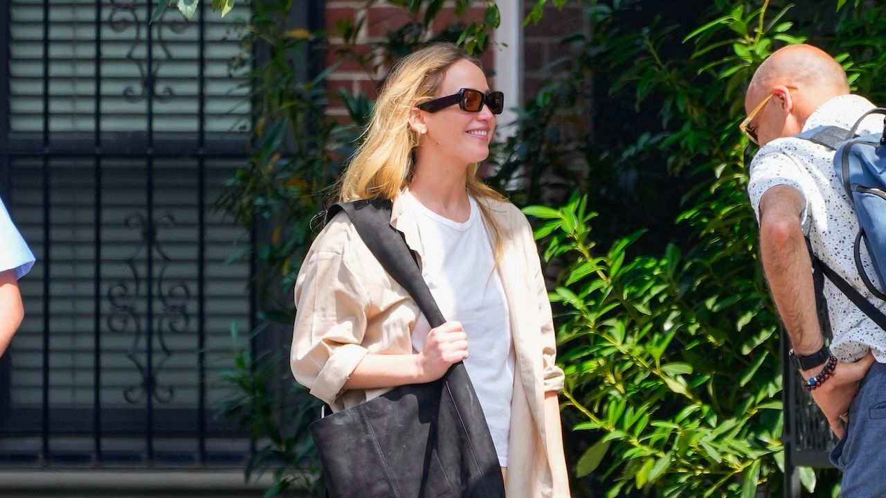 Jennifer Lawrence wearing a white tee, beige button-down, butter yellow parachute pants, and maxi black tote bag while out in New York City June 2024