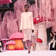A model walks the runway surrounded by oversize mushrooms and pink leaves