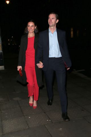 Pippa Middleton wears a long red dress and matching pumps while her husband James Matthews wears a black suit with a light blue shirt underneath