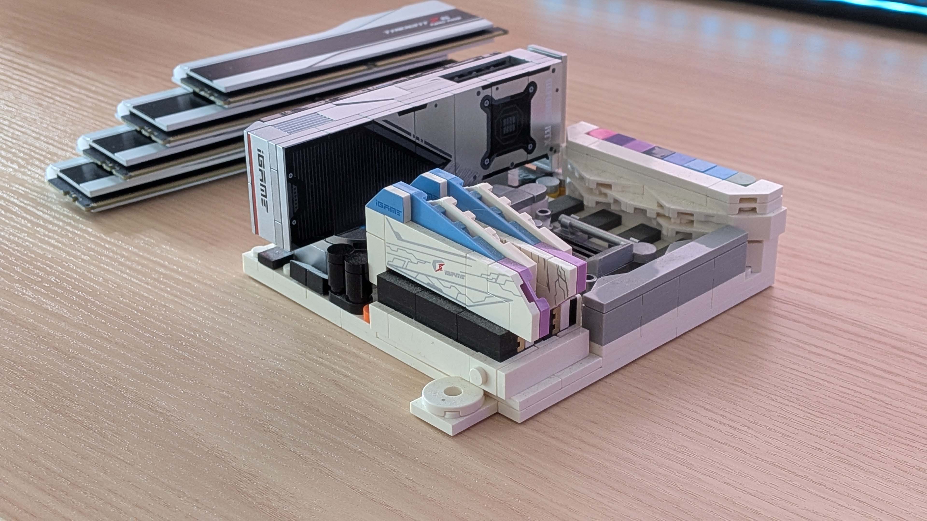 A Colorful bricks motherboard, RAM, and GPU, with a stack of real memory in the background
