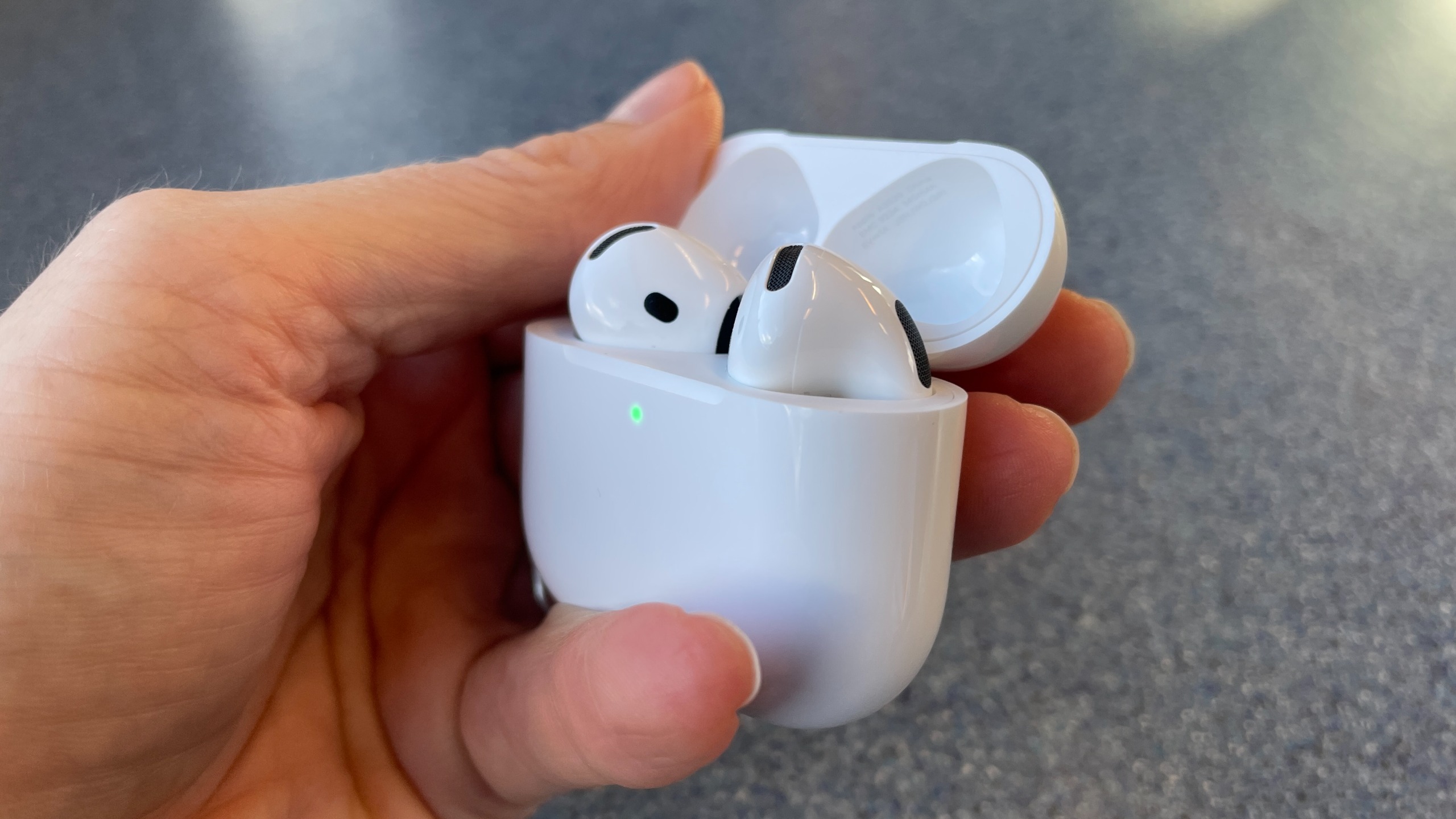 Apple AirPods 5 with Wireless Charging, on a blue table and held in a hand 