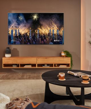 A wall-mounted Samsung's The Frame television with wooden sideboard, round coffee table, and coffee cup decor