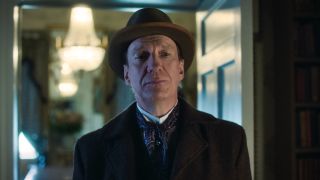 David Thewlis' Sherlock Holmes standing in front of open door inside a house