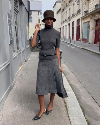 fashion influencer Sylvie Mus wearing a grey midi skirt, turtleneck knit top, slingback pumps, and a skinny belt