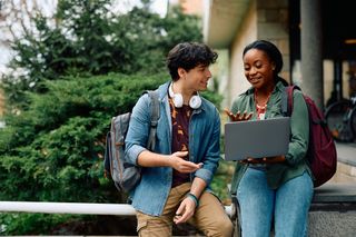 Two university students talking between a laptop.