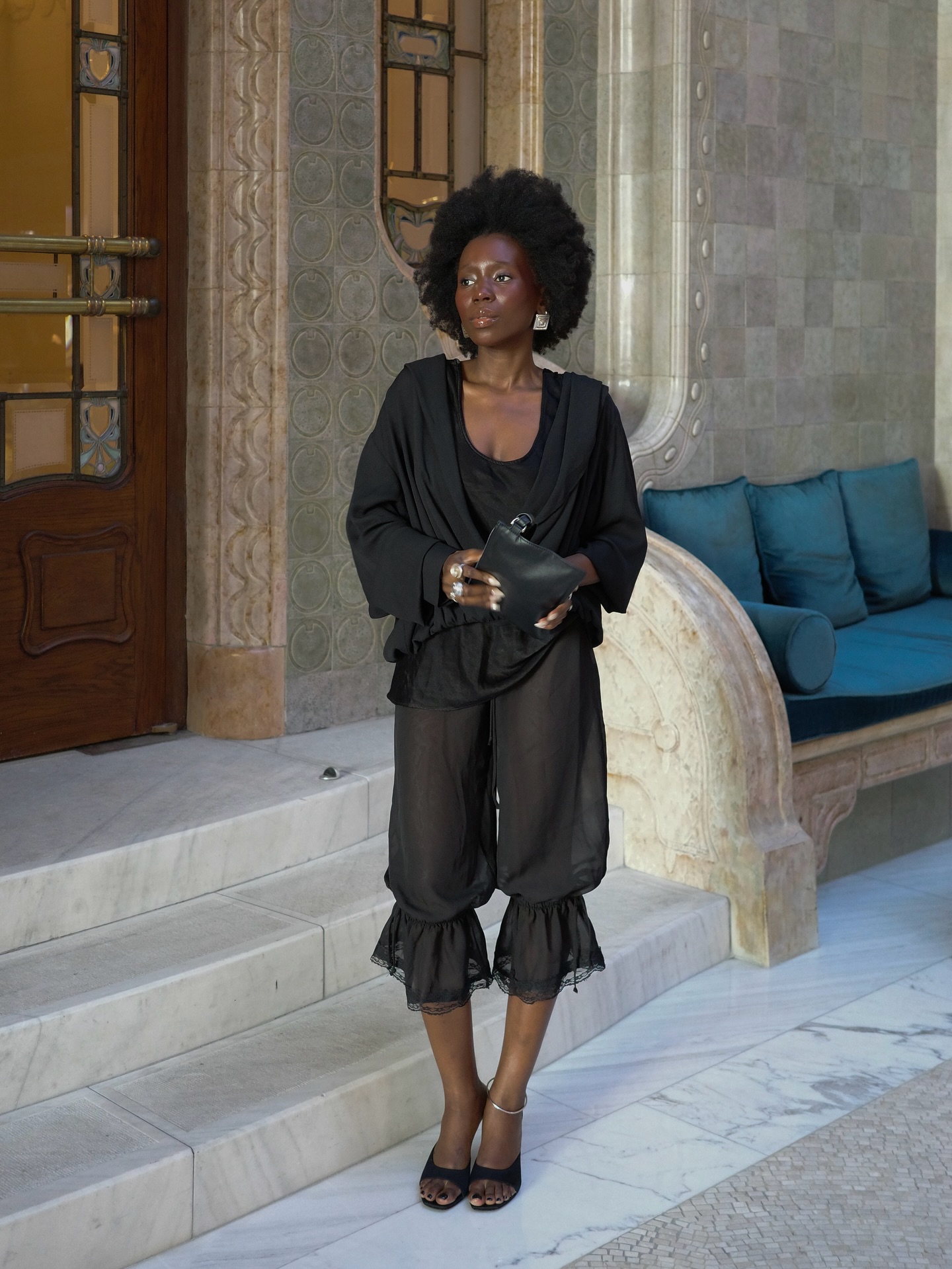 An image of @daniellejinadu wearing black trousers with black heels with a draped blouse whilst in London.