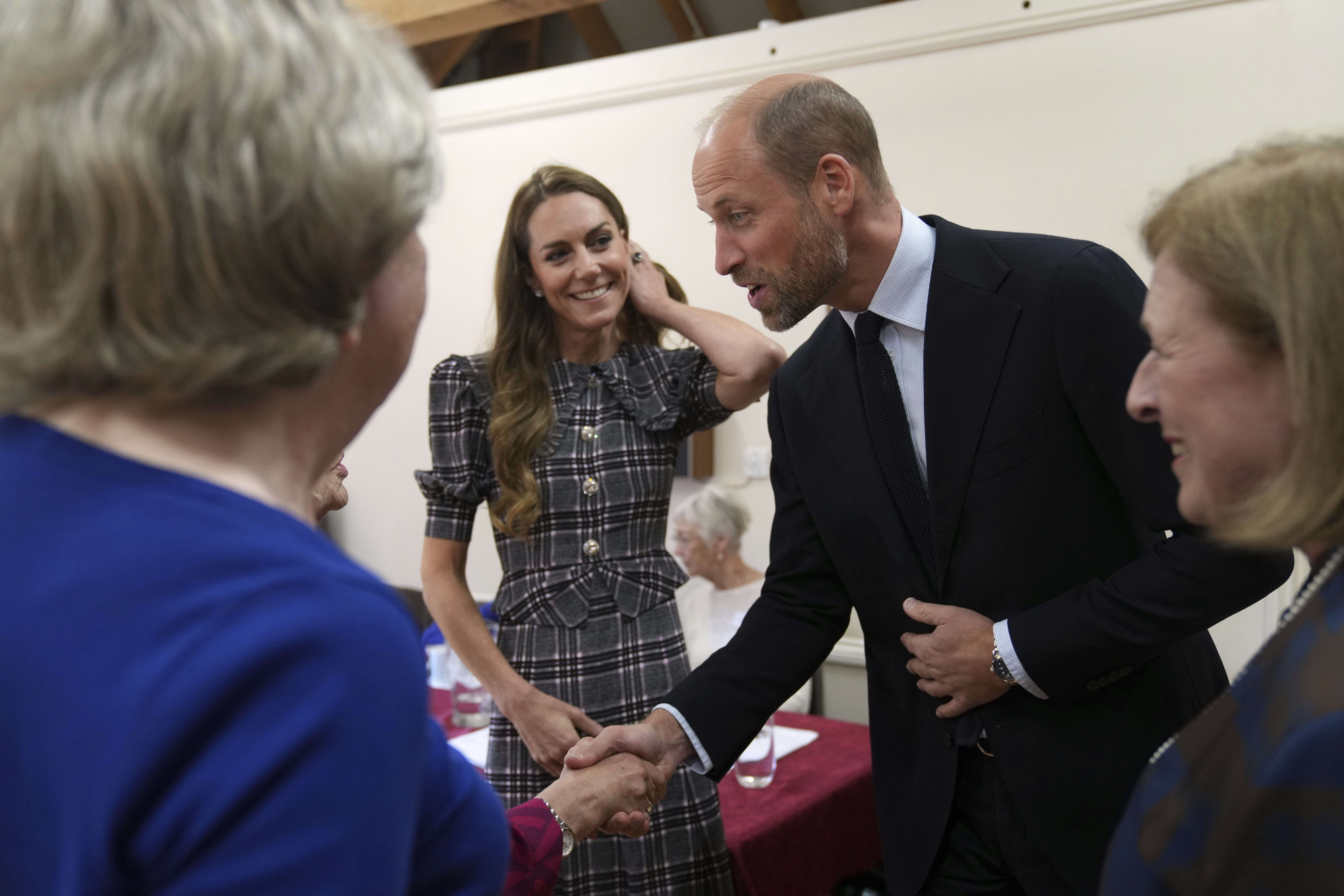 Kate Middleton wearing a gray plaid dress and smiling next to Prince William and a group of older women