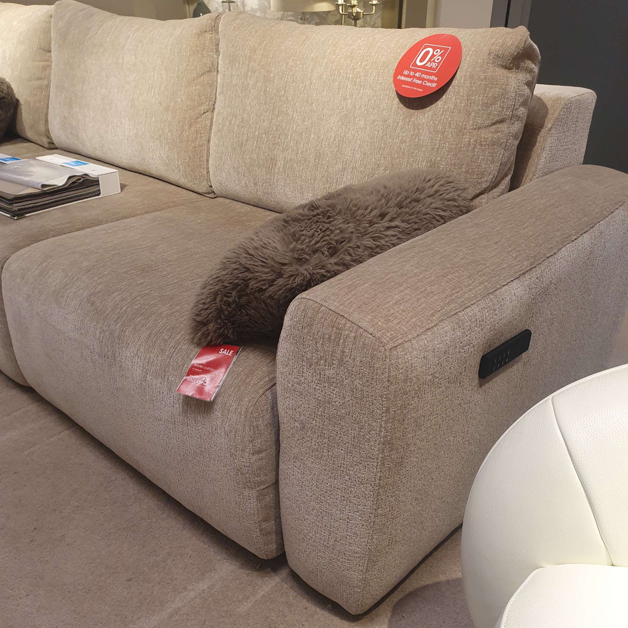 The side of the Ideal Home Gemini sofa in beige at a Furniture Village store with a remote control magnetically attached to it