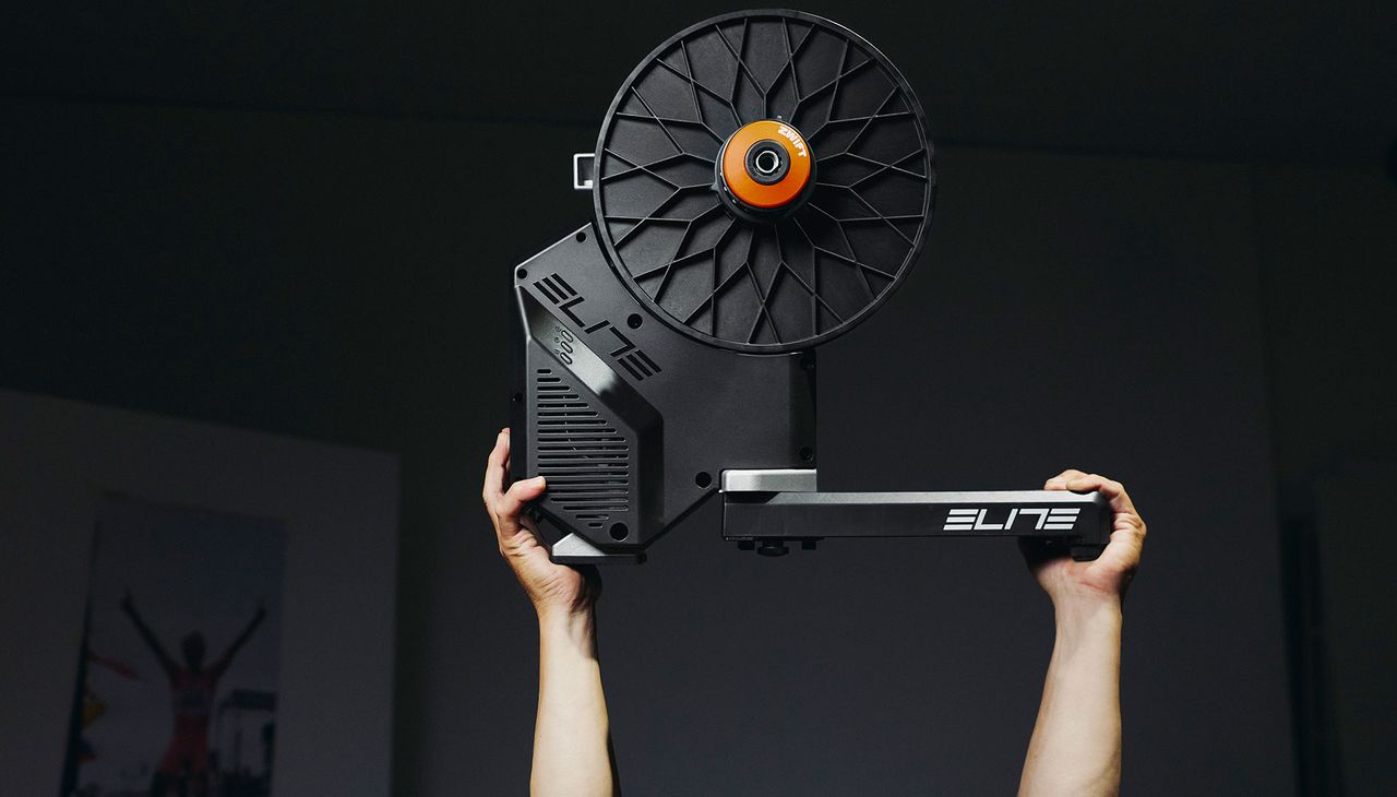 Elite Rivo with Zwift Cog and Click being held aloft by two hands
