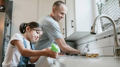 A dad and his little girl clean the kitchen together.