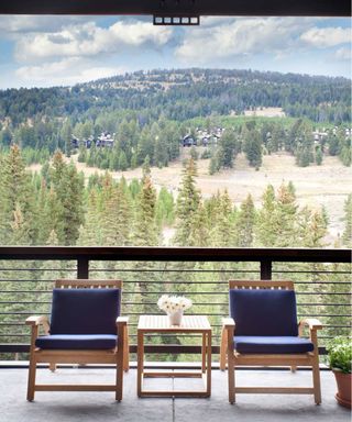 A balcony with wooded, hilly views and a wooden table and chair set with navy blue cushions.