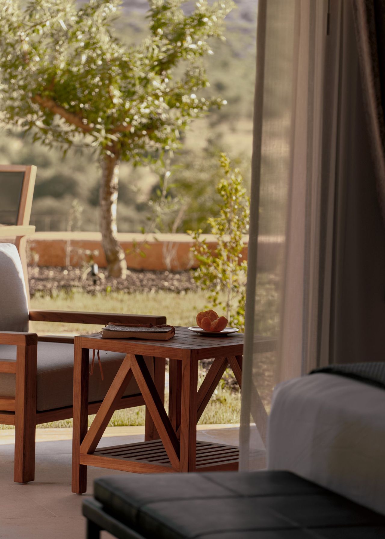 Outdoor furniture has been placed just outside the bedroom. The door remains open with a view of a chair and table as well as a large green tree.