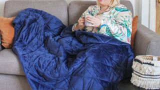Woman in pyjamas on sofa with blue Kudd.ly Weighted Blanket