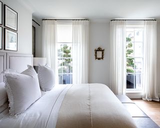 Light bedroom ideas featuring a white bed next to two large windows with white drapes