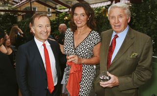 Tony Chambers (left) wearing a black suit with a bright red tie. Centre: Catherine Fairweather wearing a black dress and white dress: Right: Sir Don McCullin wearing a brown suit, with red tie holding a drink.