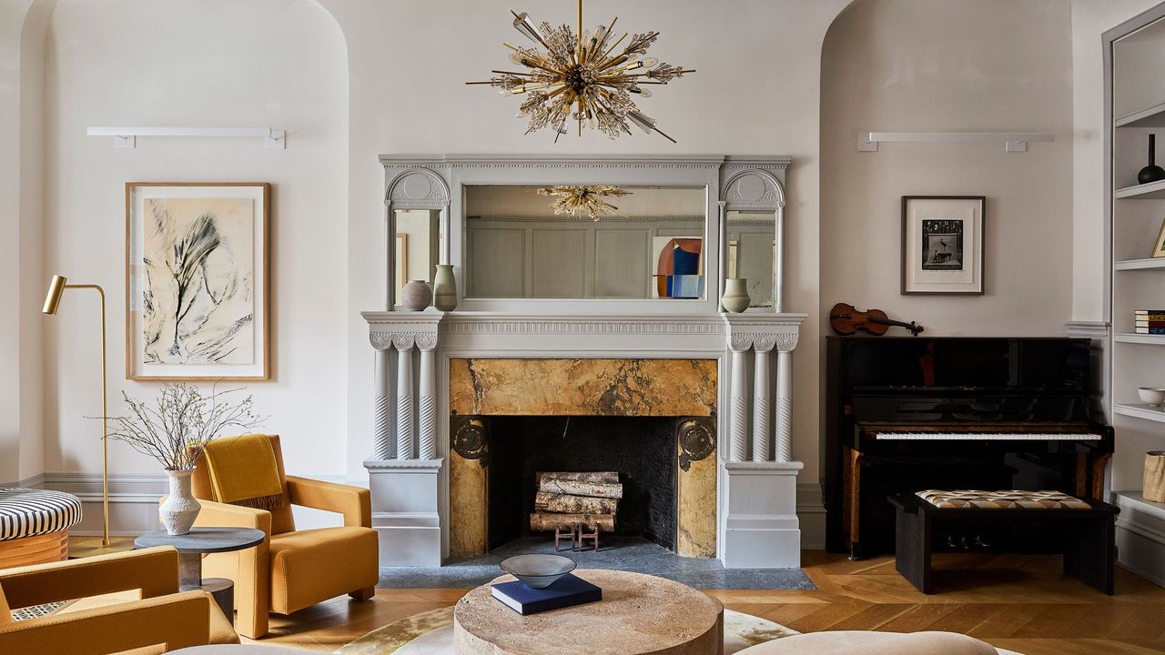 elegant living room with piano, marble fireplace, amber armchairs, statement pendant light and round coffee table