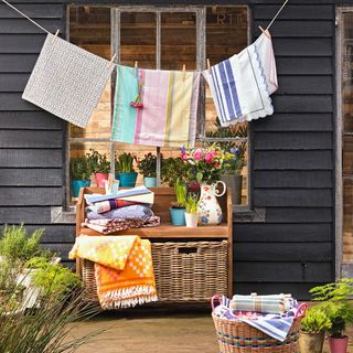 Colourful cloths hanging on line above wicker baskets and potted plants outside.