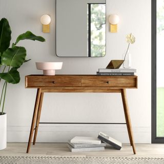 a stylish ntryway console table with decor including lamps, a mirror, and books on the floor