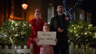 Roy and Kelley standing behind Pheobe who is holding a sign that says "say it's carol singers."