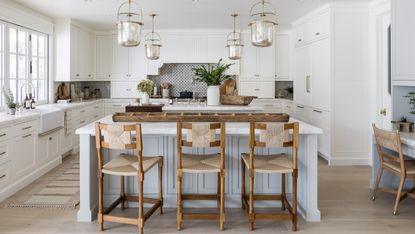 white kitchen with light gray island, gold pendants and wooden and rattan bar stools