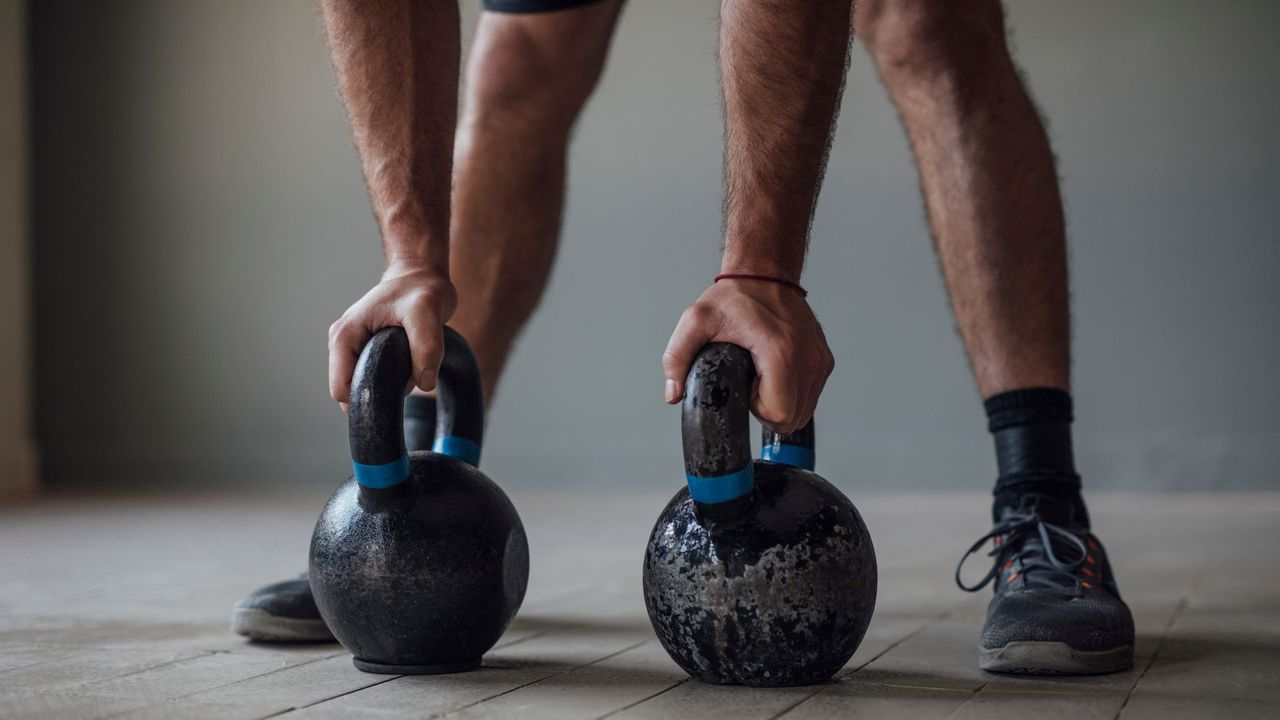 Two kettlebells on the floor with a man&#039;s hands on either one