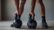 Two kettlebells on the floor with a man's hands on either one