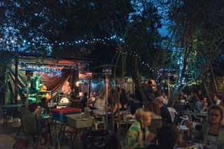 An outdoor nightlife venue features glowing fairy lights as a band plays live.