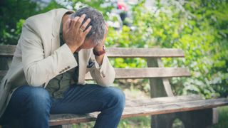 Man sitting on park bench with head in hands